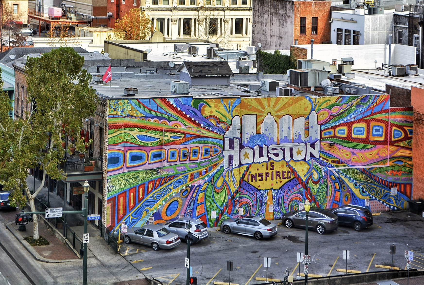 A colorful Houston mural reading “Houston Is Inspired,” painted across a full building wall, with swirling patterns and radiating lines symbolizing community creativity and cultural vibrancy.
